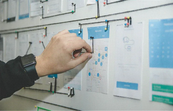 Title: Hand pinning printed page plans and wireframes to a wall during content planning - Description: Hand pinning printed page plans and wireframes to a wall during content planning